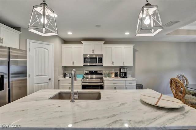 kitchen featuring stainless steel appliances, hanging light fixtures, a sink, and light stone countertops