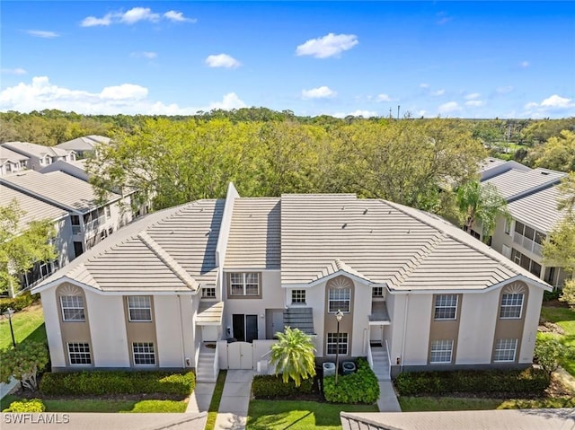 view of front of house with a wooded view, a tile roof, and stucco siding