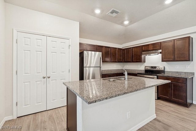 kitchen featuring light stone counters, a kitchen island with sink, under cabinet range hood, a sink, and appliances with stainless steel finishes