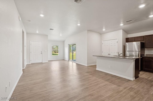 kitchen with light wood-style floors, open floor plan, a kitchen island with sink, and dark brown cabinetry