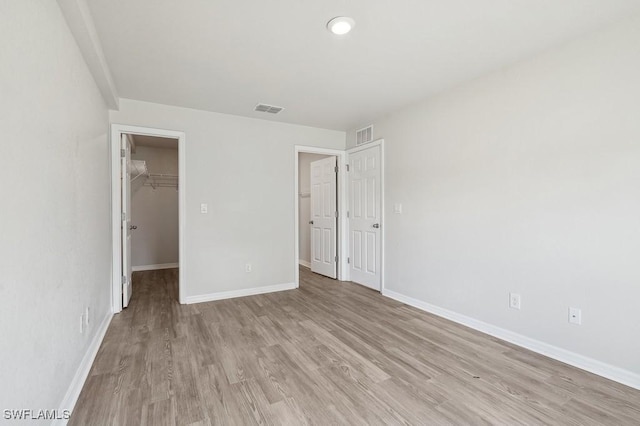 unfurnished bedroom featuring light wood finished floors, visible vents, a spacious closet, and baseboards