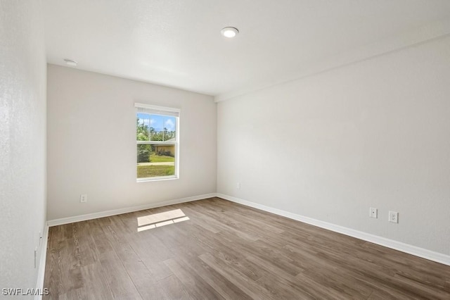 spare room with baseboards and wood finished floors