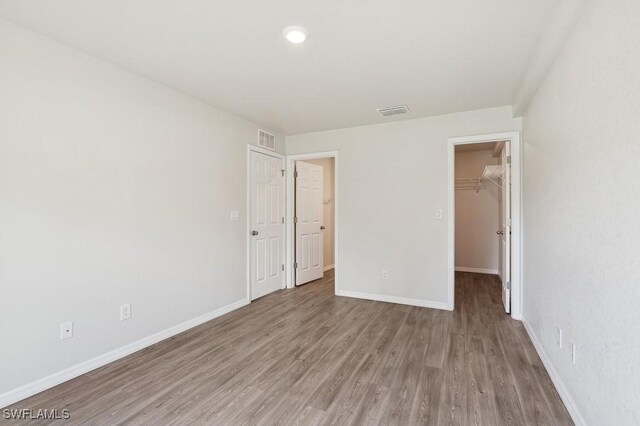 unfurnished bedroom featuring light wood-type flooring, baseboards, visible vents, and a walk in closet