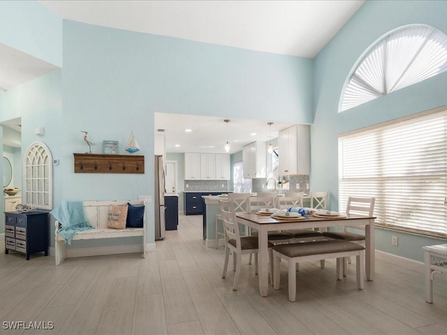 dining space with light wood-type flooring, a towering ceiling, and baseboards