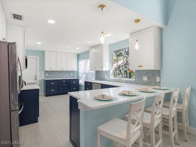 kitchen featuring blue cabinets, stainless steel appliances, white cabinetry, hanging light fixtures, and a kitchen bar