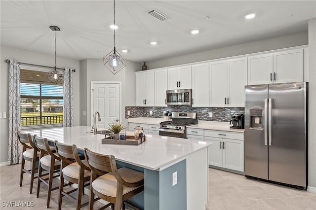 kitchen with a center island with sink, tasteful backsplash, white cabinetry, appliances with stainless steel finishes, and light countertops