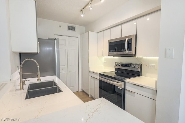 kitchen with visible vents, appliances with stainless steel finishes, light stone counters, white cabinetry, and a sink