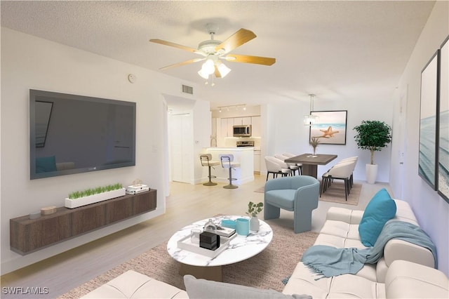 living area featuring a textured ceiling, ceiling fan, light wood finished floors, and visible vents