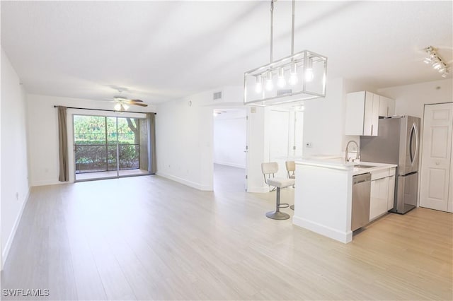 kitchen featuring stainless steel appliances, light countertops, light wood-style floors, white cabinetry, and a sink