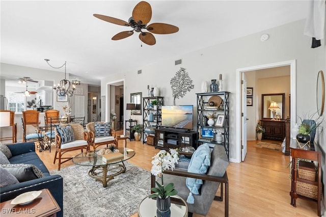 living area with ceiling fan with notable chandelier, visible vents, light wood finished floors, and baseboards