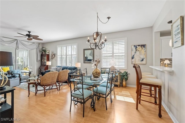 dining room featuring plenty of natural light, ceiling fan with notable chandelier, light wood-type flooring, and baseboards