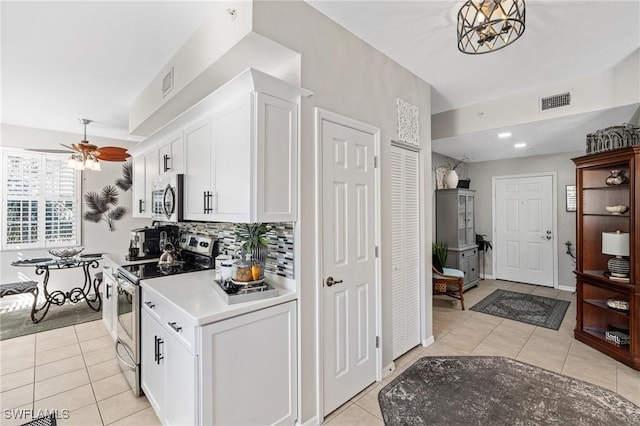 kitchen with decorative backsplash, light tile patterned flooring, white cabinets, stainless steel appliances, and a ceiling fan