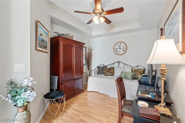 bedroom with a tray ceiling, baseboards, light wood finished floors, and ceiling fan