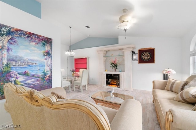 living area with vaulted ceiling, light wood finished floors, a fireplace, and a notable chandelier