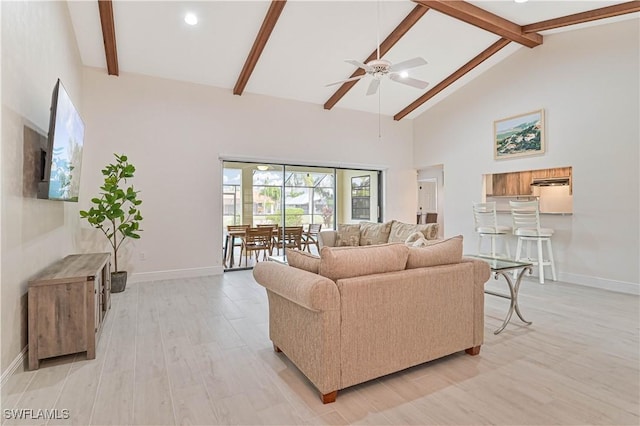 living area with baseboards, a ceiling fan, beamed ceiling, light wood-type flooring, and high vaulted ceiling