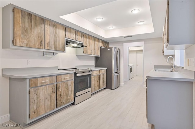 kitchen featuring a tray ceiling, stainless steel appliances, light countertops, under cabinet range hood, and a sink