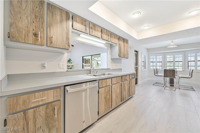 kitchen with a raised ceiling, light countertops, stainless steel dishwasher, light wood-style floors, and a sink