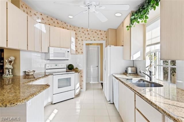 kitchen featuring light tile patterned floors, a sink, white appliances, a peninsula, and wallpapered walls