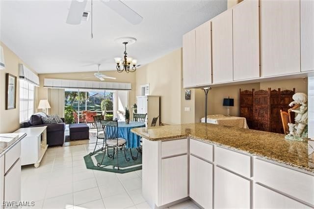 kitchen with open floor plan, vaulted ceiling, light stone countertops, a peninsula, and ceiling fan with notable chandelier