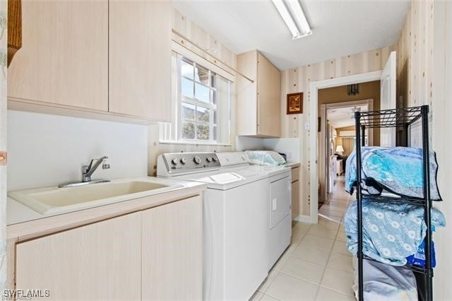 clothes washing area with light tile patterned floors, washer and clothes dryer, a sink, and cabinet space