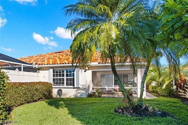 rear view of property with a yard, a tile roof, a sunroom, and stucco siding