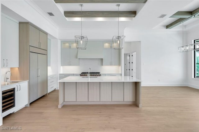 kitchen featuring wine cooler, paneled built in refrigerator, light countertops, a center island with sink, and pendant lighting