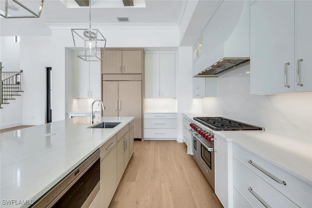 kitchen with premium appliances, light stone counters, decorative light fixtures, a sink, and premium range hood