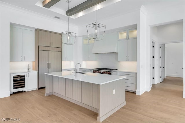 kitchen featuring a kitchen island with sink, beverage cooler, paneled built in refrigerator, light countertops, and glass insert cabinets