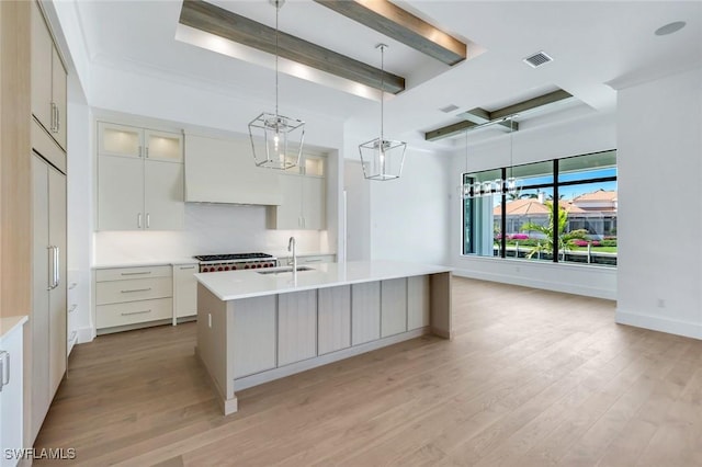 kitchen with a kitchen island with sink, glass insert cabinets, light countertops, and a sink