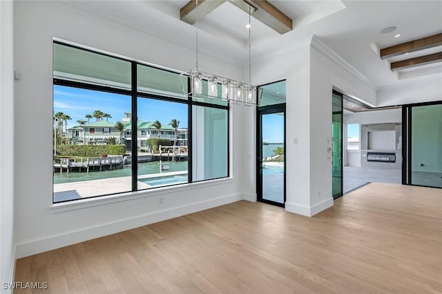 empty room featuring a water view, beamed ceiling, light wood-style flooring, and baseboards