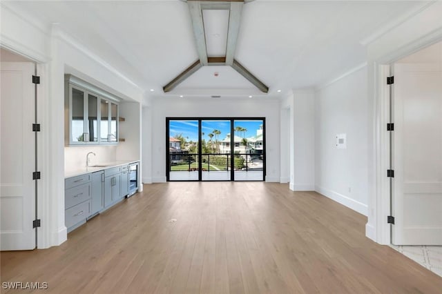 unfurnished living room with baseboards, wine cooler, a sink, and light wood-style floors