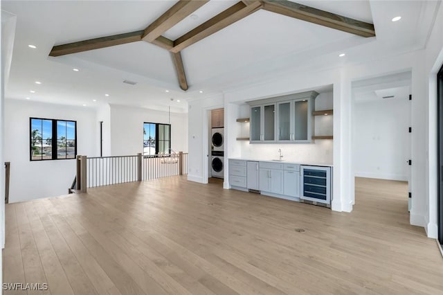 unfurnished living room featuring vaulted ceiling with beams, wine cooler, light wood-style flooring, stacked washer / dryer, and indoor wet bar