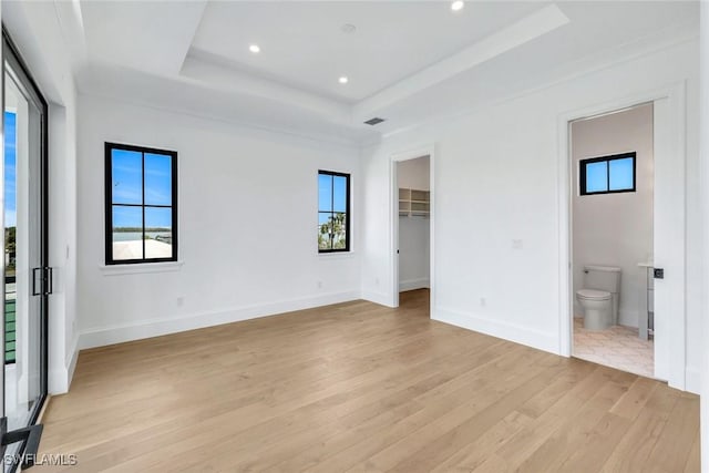 unfurnished bedroom featuring light wood-type flooring, baseboards, multiple windows, and a tray ceiling