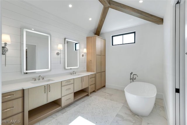 full bathroom featuring marble finish floor, a freestanding bath, beam ceiling, and a sink