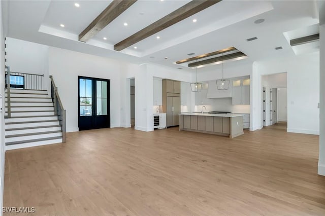 unfurnished living room with a towering ceiling, light wood-style floors, french doors, stairway, and beamed ceiling