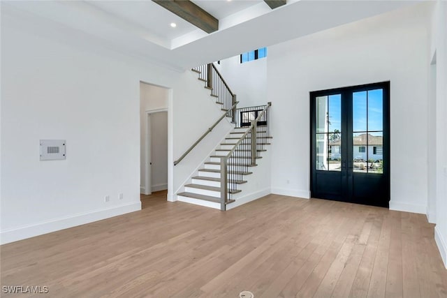 entrance foyer with beam ceiling, french doors, stairway, light wood-style flooring, and baseboards