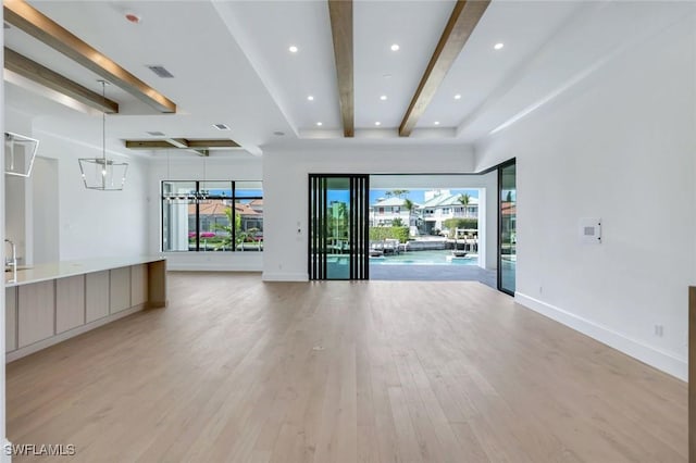 spare room featuring a healthy amount of sunlight, light wood finished floors, baseboards, and beamed ceiling