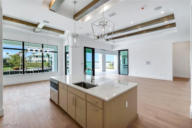 kitchen featuring beam ceiling, light brown cabinetry, open floor plan, a kitchen island with sink, and a sink