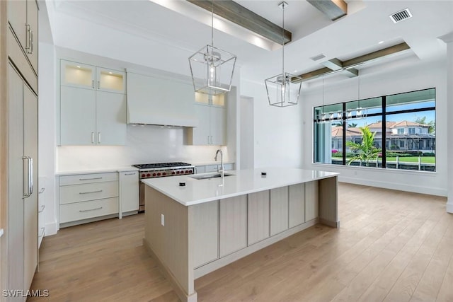 kitchen featuring stainless steel stove, light countertops, glass insert cabinets, a kitchen island with sink, and a sink