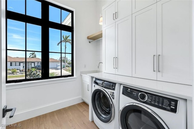 washroom featuring light wood-type flooring, baseboards, cabinet space, and washing machine and clothes dryer