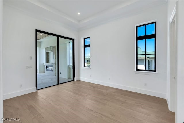 empty room with light wood finished floors, baseboards, a raised ceiling, and recessed lighting