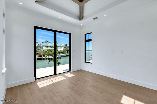 spare room featuring a tray ceiling, light wood finished floors, a water view, and baseboards