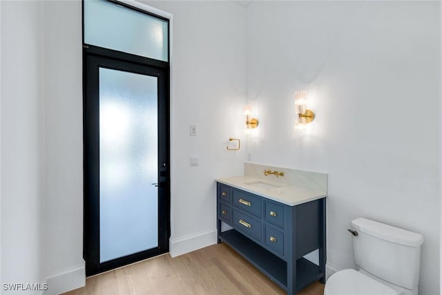 bathroom featuring toilet, baseboards, wood finished floors, and vanity