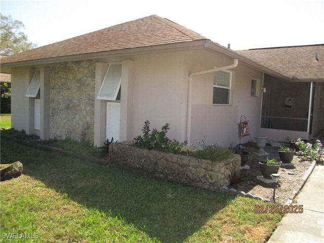 view of property exterior featuring a yard, stucco siding, a shingled roof, a sunroom, and stone siding