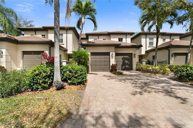 view of front facade featuring a garage, a tiled roof, decorative driveway, and stucco siding