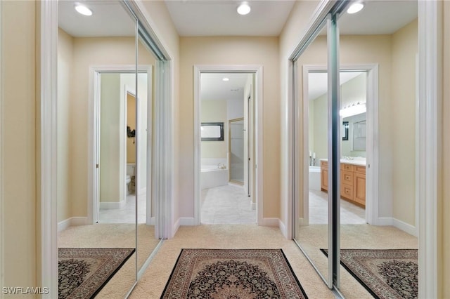 corridor featuring light colored carpet and baseboards