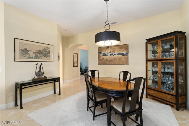 dining space with arched walkways, light tile patterned floors, visible vents, and baseboards