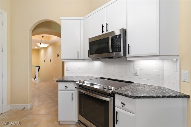 kitchen featuring tasteful backsplash, arched walkways, white cabinets, dark stone counters, and appliances with stainless steel finishes