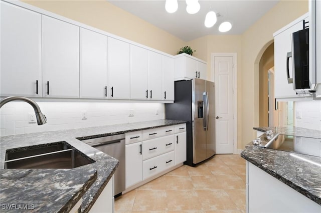 kitchen with arched walkways, decorative backsplash, appliances with stainless steel finishes, a sink, and dark stone counters