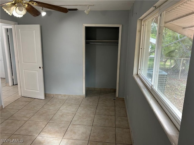 unfurnished bedroom featuring light tile patterned flooring, a ceiling fan, baseboards, a closet, and rail lighting